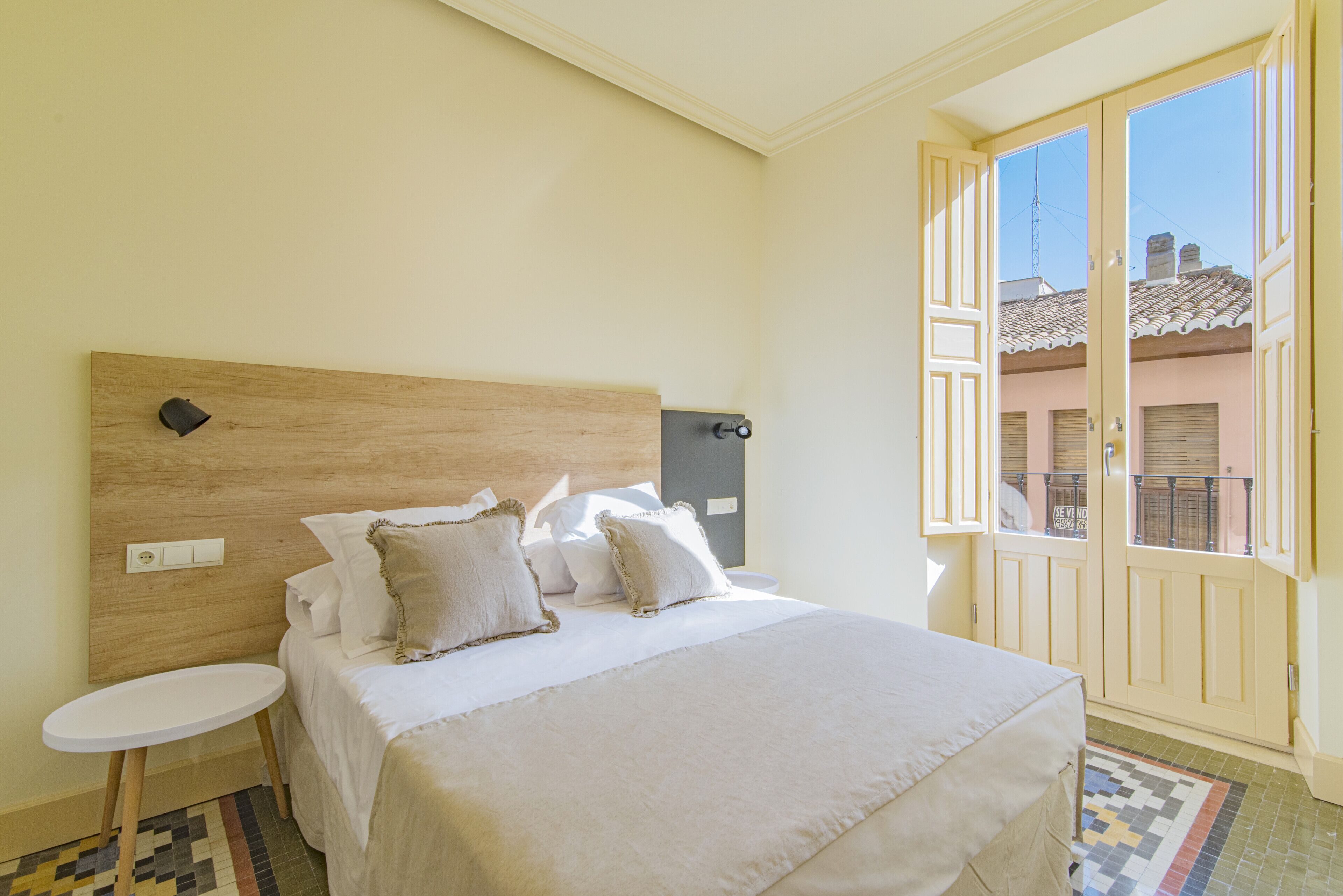 A bedroom with a wooden headboard, a small bedside table, and a large bed with multiple pillows.
