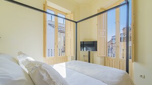 Un dormitorio con dos camas, televisión y ventanas amplias con persianas de madera.