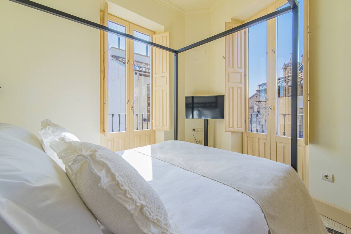 Un dormitorio con dos camas, televisión y ventanas amplias con persianas de madera.