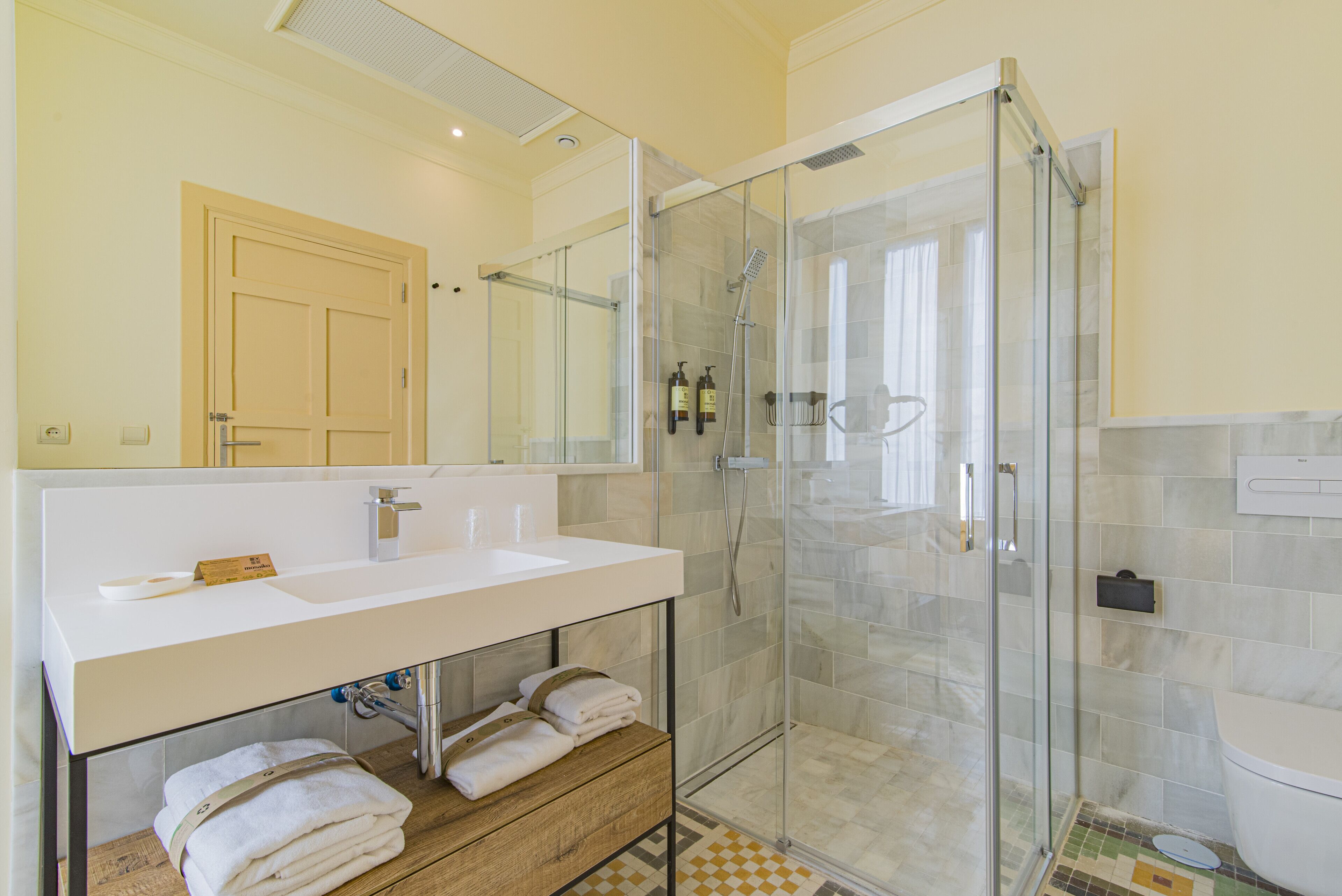 Ein modernes Badezimmer mit einer gläsernen Duschkabine, einem weißen Waschbecken und einem Holfach darunter.