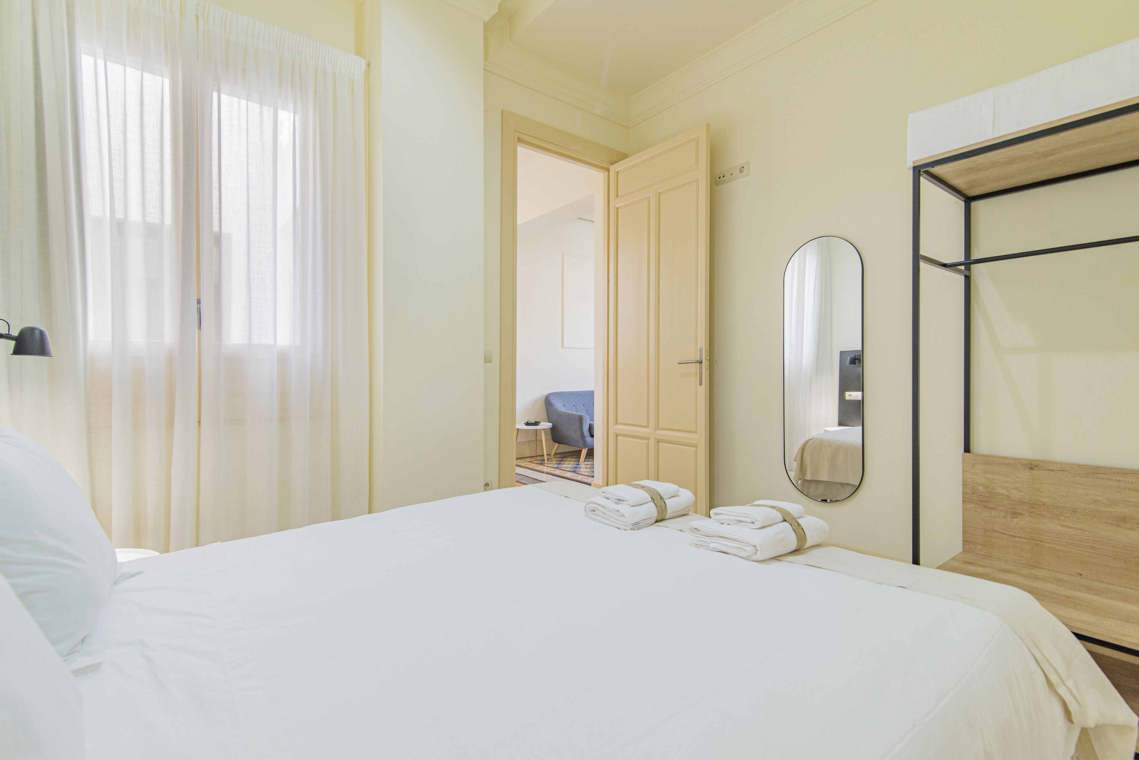 A hotel room with a large bed, a wooden headboard, a mirror, and a door leading to another room.