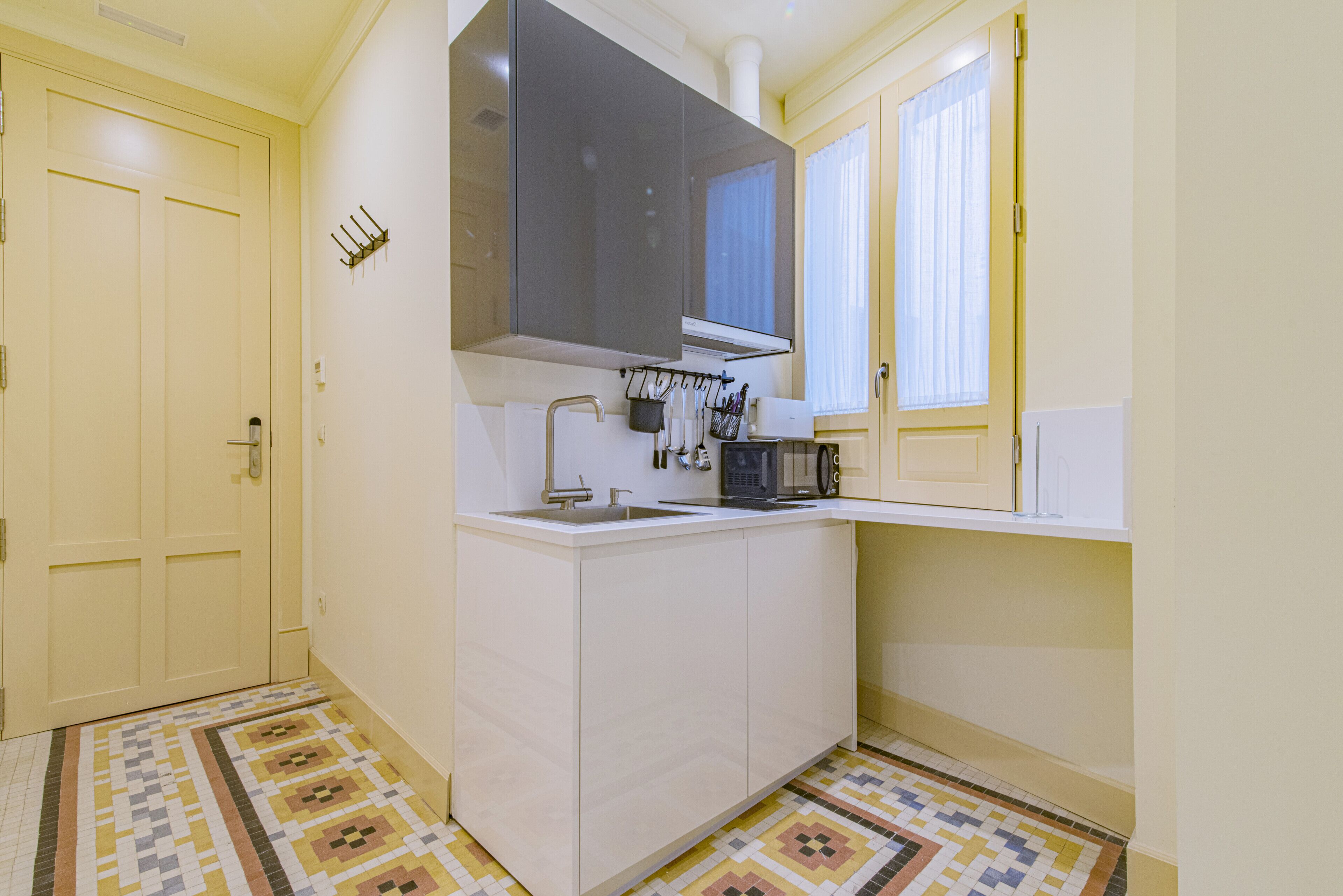 Una cocina compacta con microondas integrado, un lavamanos y una ventana con cortinas.