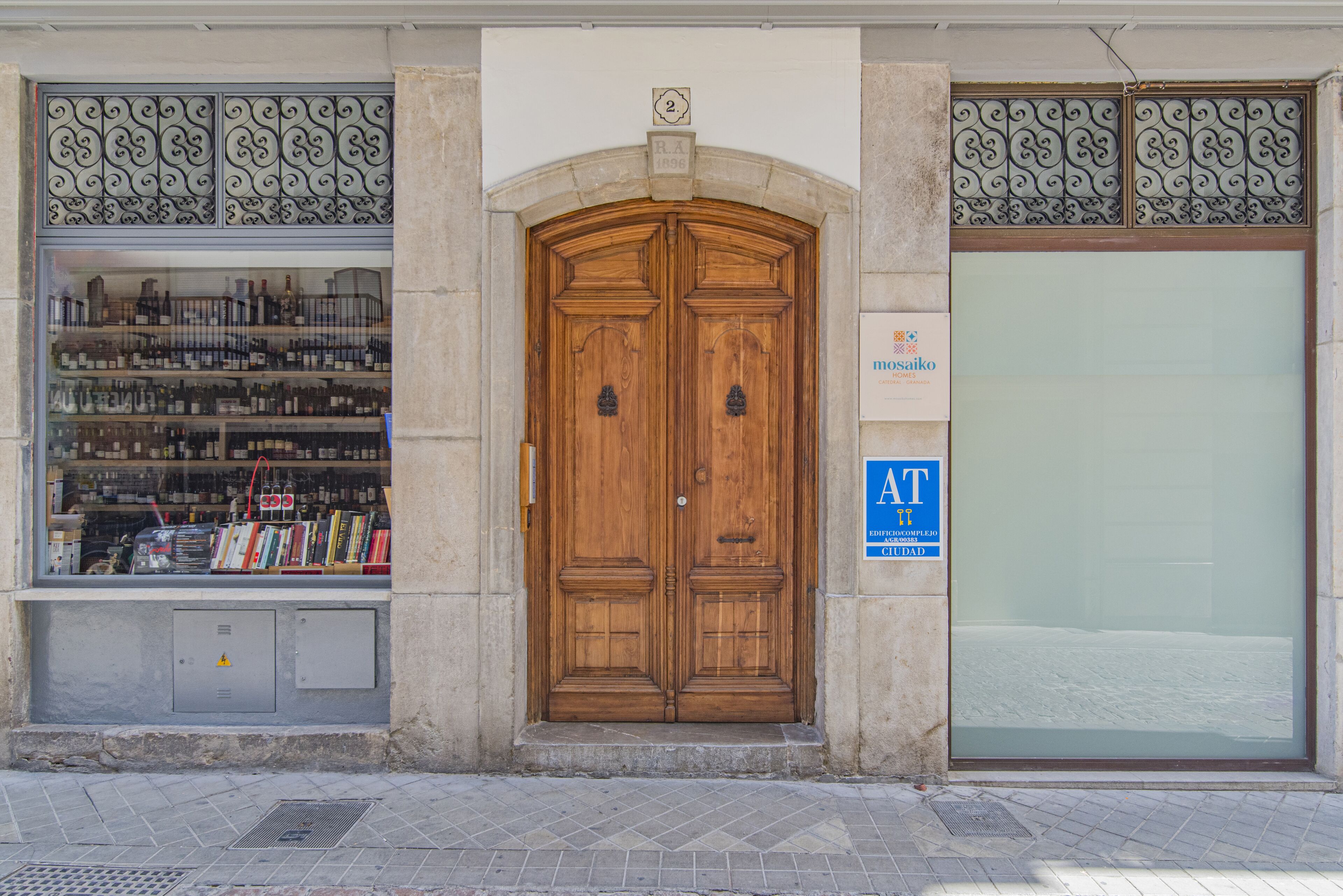 Una puerta doble de madera con un letrero encima, un ventanal con libros y botellas, y un cartel azul a la derecha.