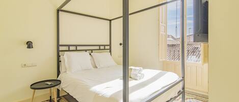 A four-poster bed with white linens, a small bedside table, and a television mounted on the wall.
