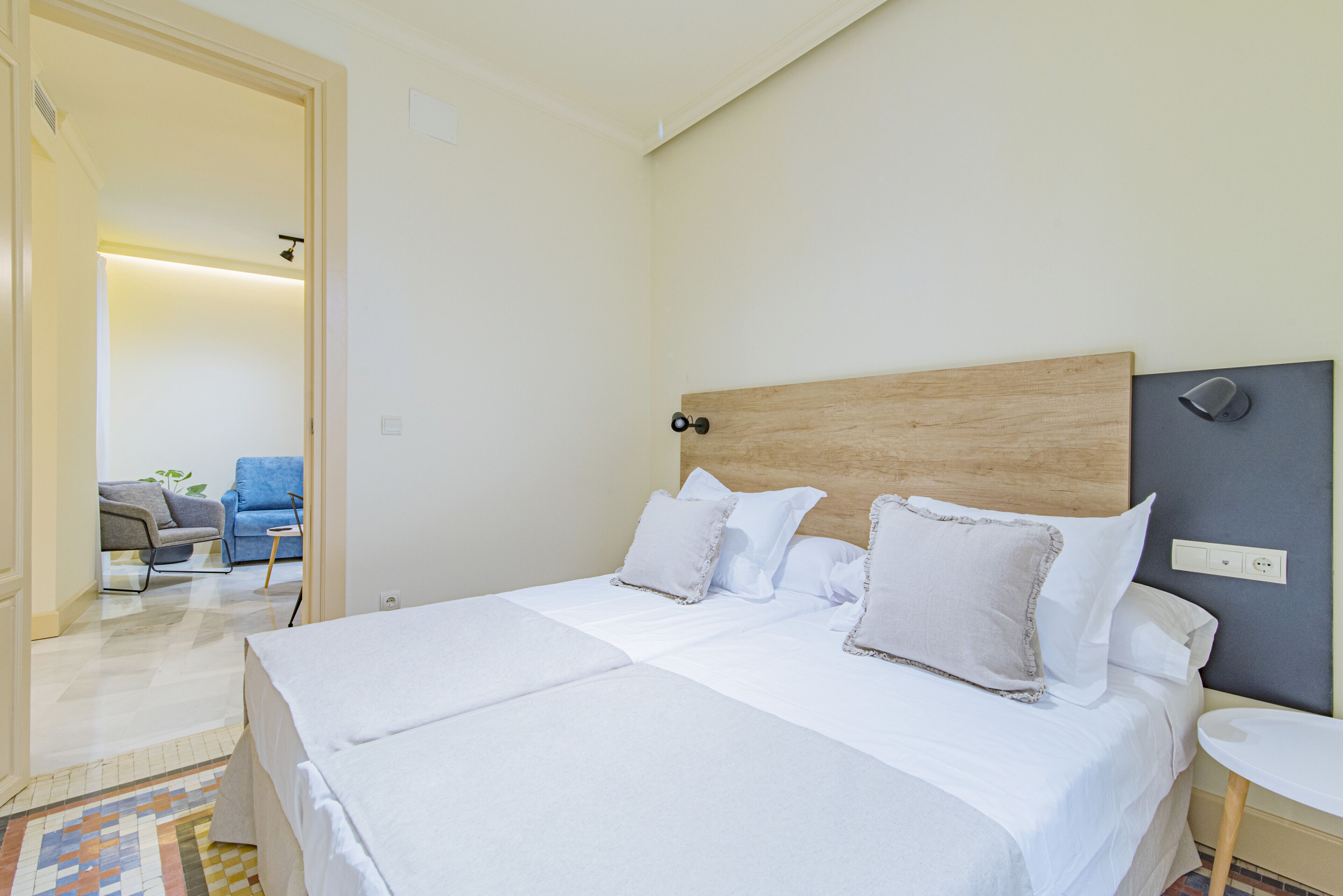 A hotel room with a large bed, a bedside table, and a chair in the background.
