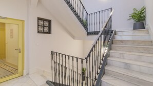 Una escalera con barandillas negras y peldaños de mármol, una planta en maceta a la derecha y una puerta con un letrero a la izquierda.