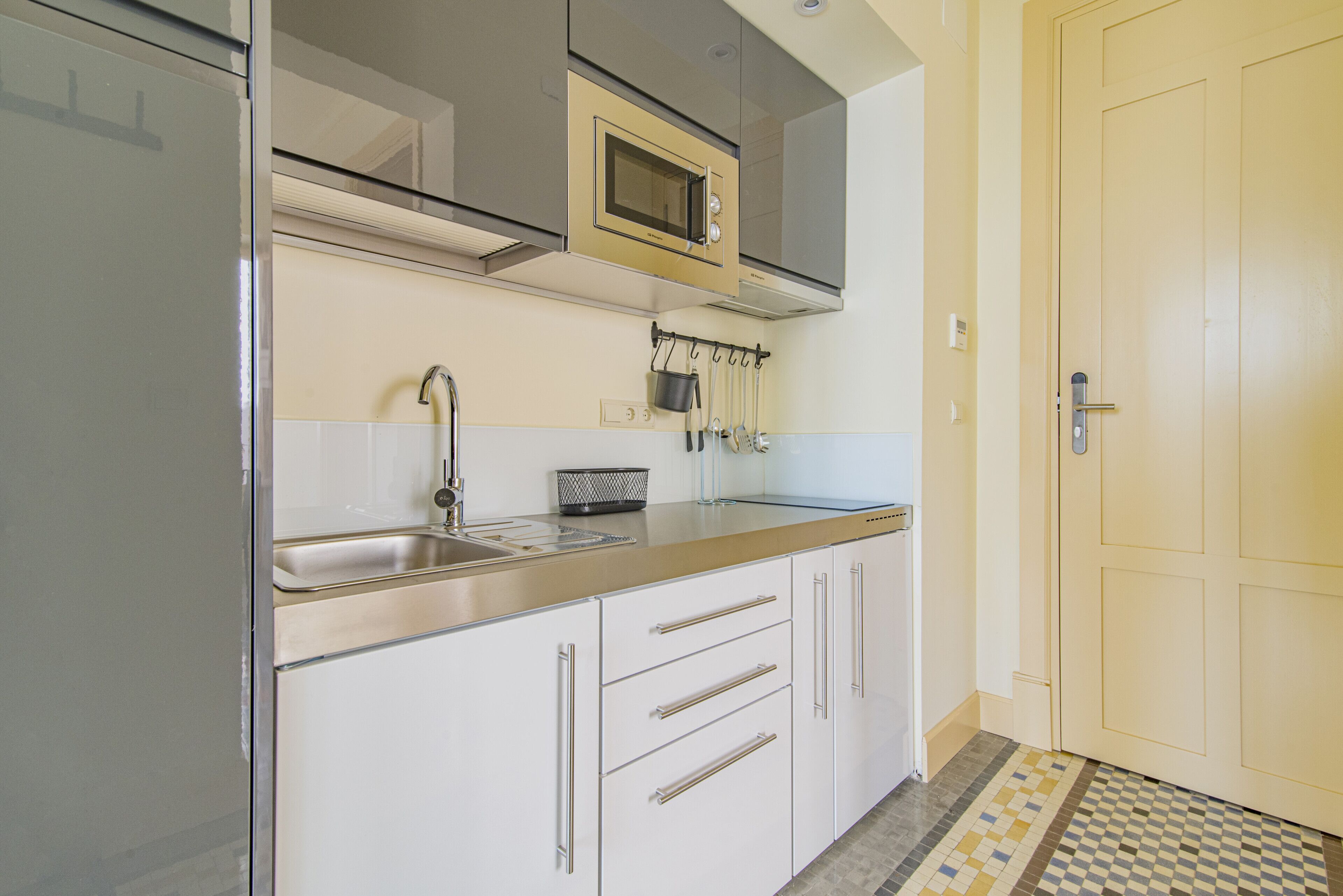 Une cuisine avec des meubles blancs, un évier en acier inoxydable, un four à micro-ondes et un tapis à motifs.
