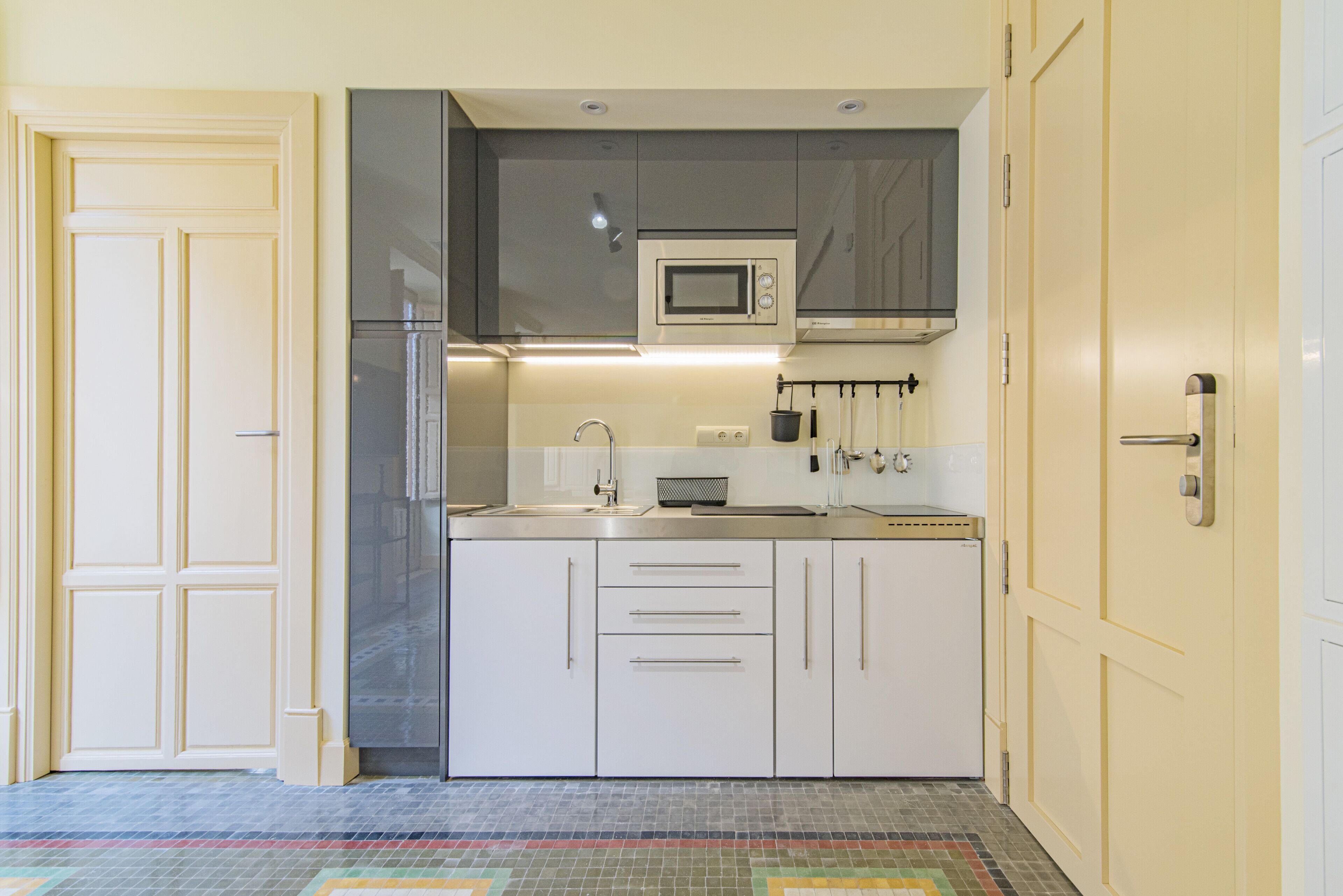 A compact kitchen with white cabinets, a stainless steel refrigerator, a microwave, and a sink.