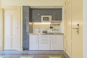 A compact kitchen with white cabinets, a stainless steel refrigerator, a microwave, and a sink.