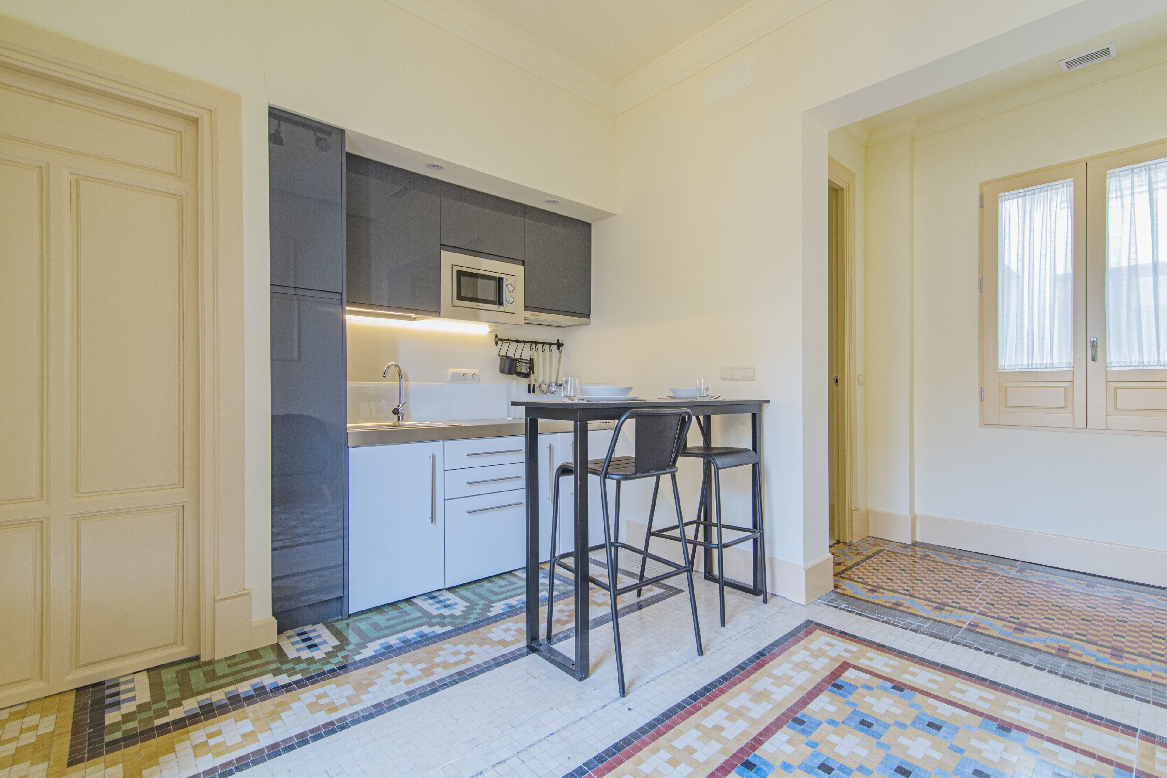 Une cuisine compacte avec des meubles blancs, un four à micro-ondes et une petite table à manger avec deux chaises.