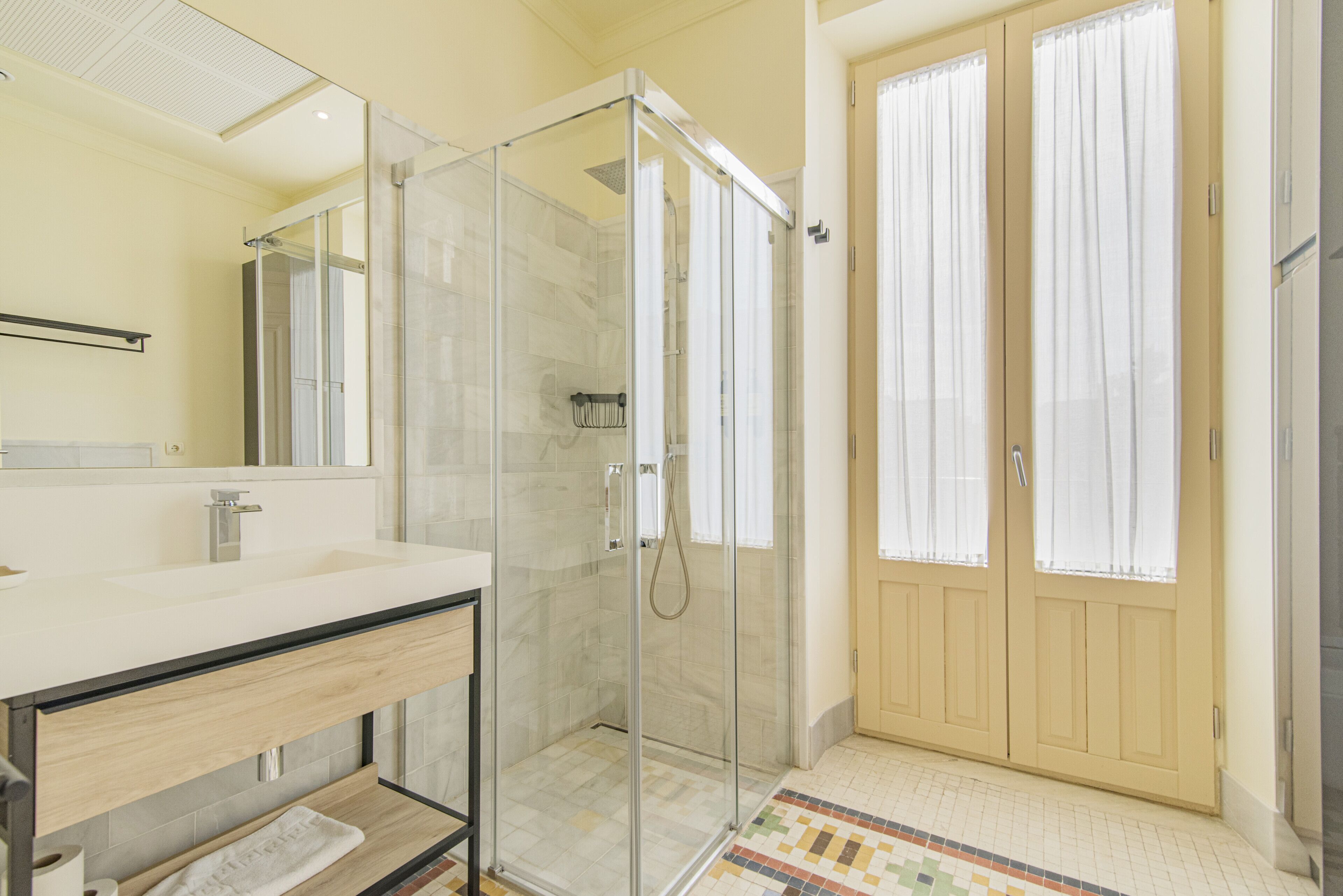 Un baño moderno con ducha envuelta en vidrio, un lavabo con tocador de madera y piso de baldosas.