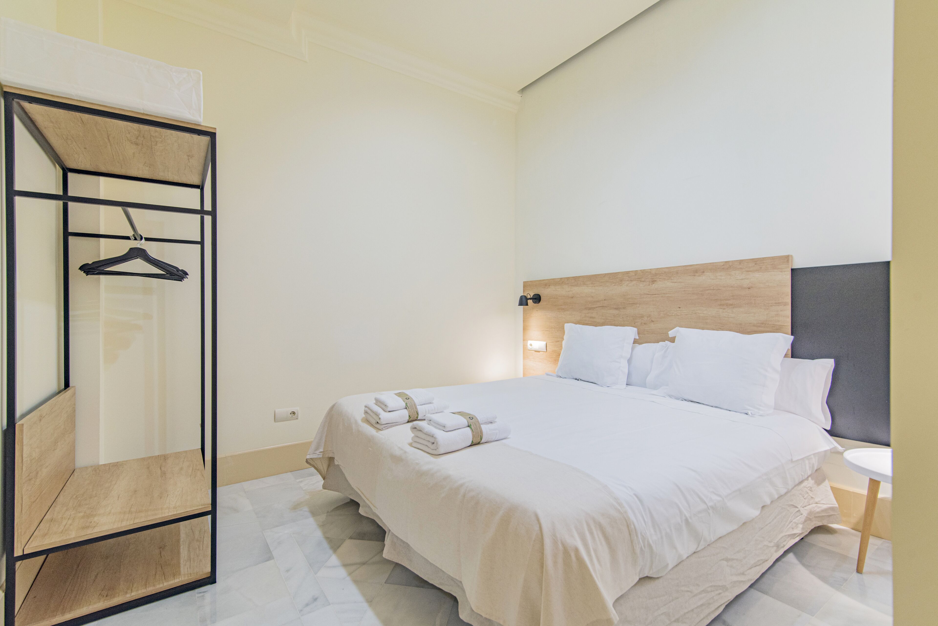 Un lit bien fait, avec du linge de lit et des serviettes blanches, une tête de lit en bois et une petite table de chevet avec une lampe.