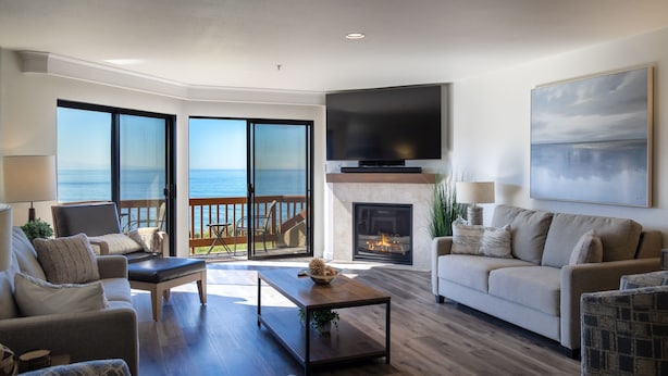 A living room with a fireplace, a television, and a view of the ocean through large sliding glass doors. - Expansive Ocean Views-Prime Condo at Seascape! (Aptos)