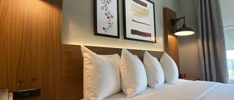 A hotel room with a large bed, wooden headboard, two framed artworks, a bedside lamp, and a nightstand with a charging station.