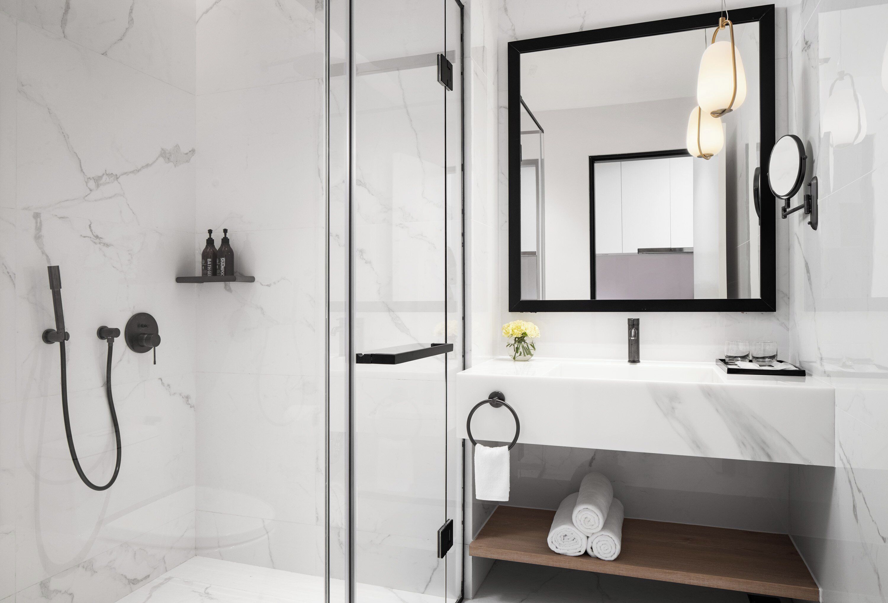 A modern bathroom with a glass-enclosed shower, a marble sink, and a mirror with a black frame.