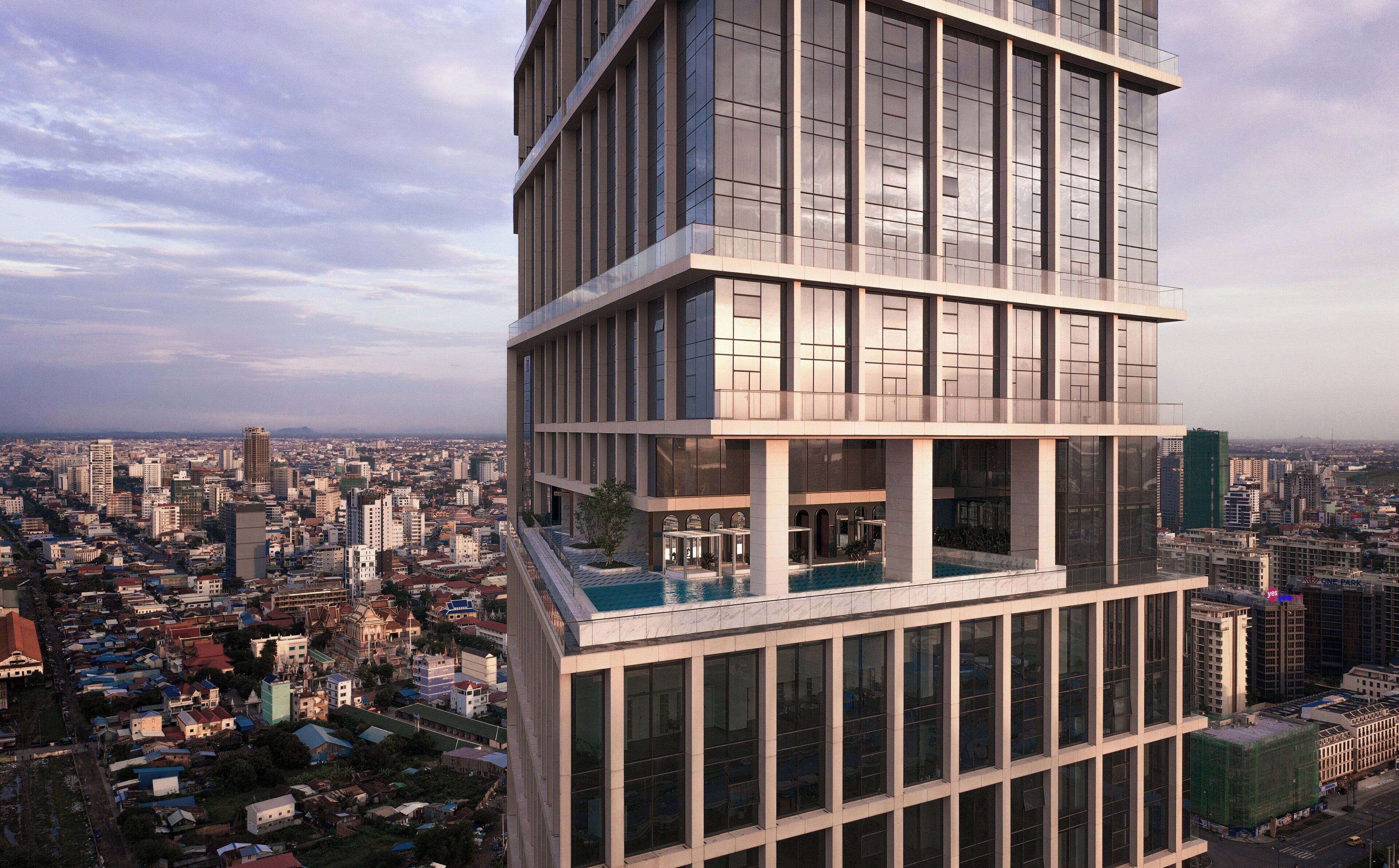 Un edificio alto con varios pisos, amplias ventanas y una piscina en la azotea.