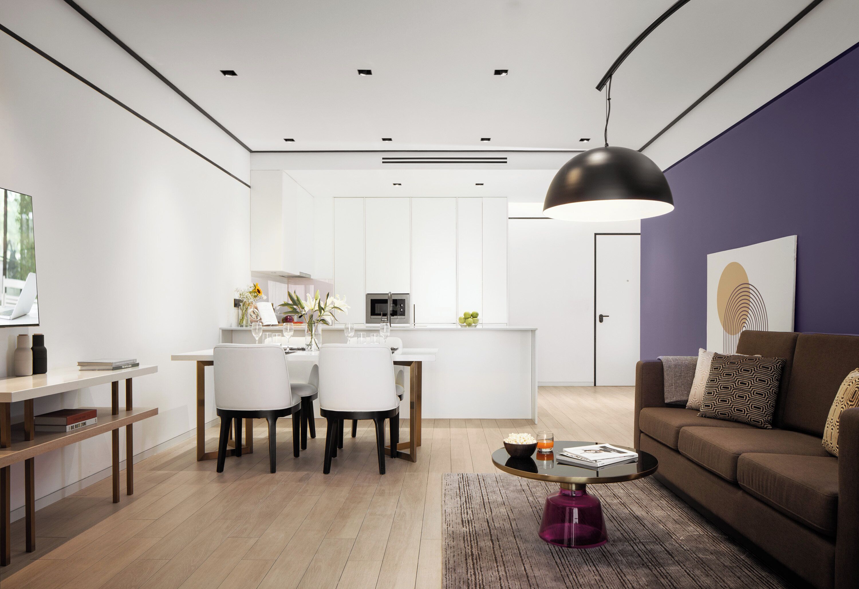 Een moderne woonkamer met een eethoek, een keuken en een paarse accentmuur.