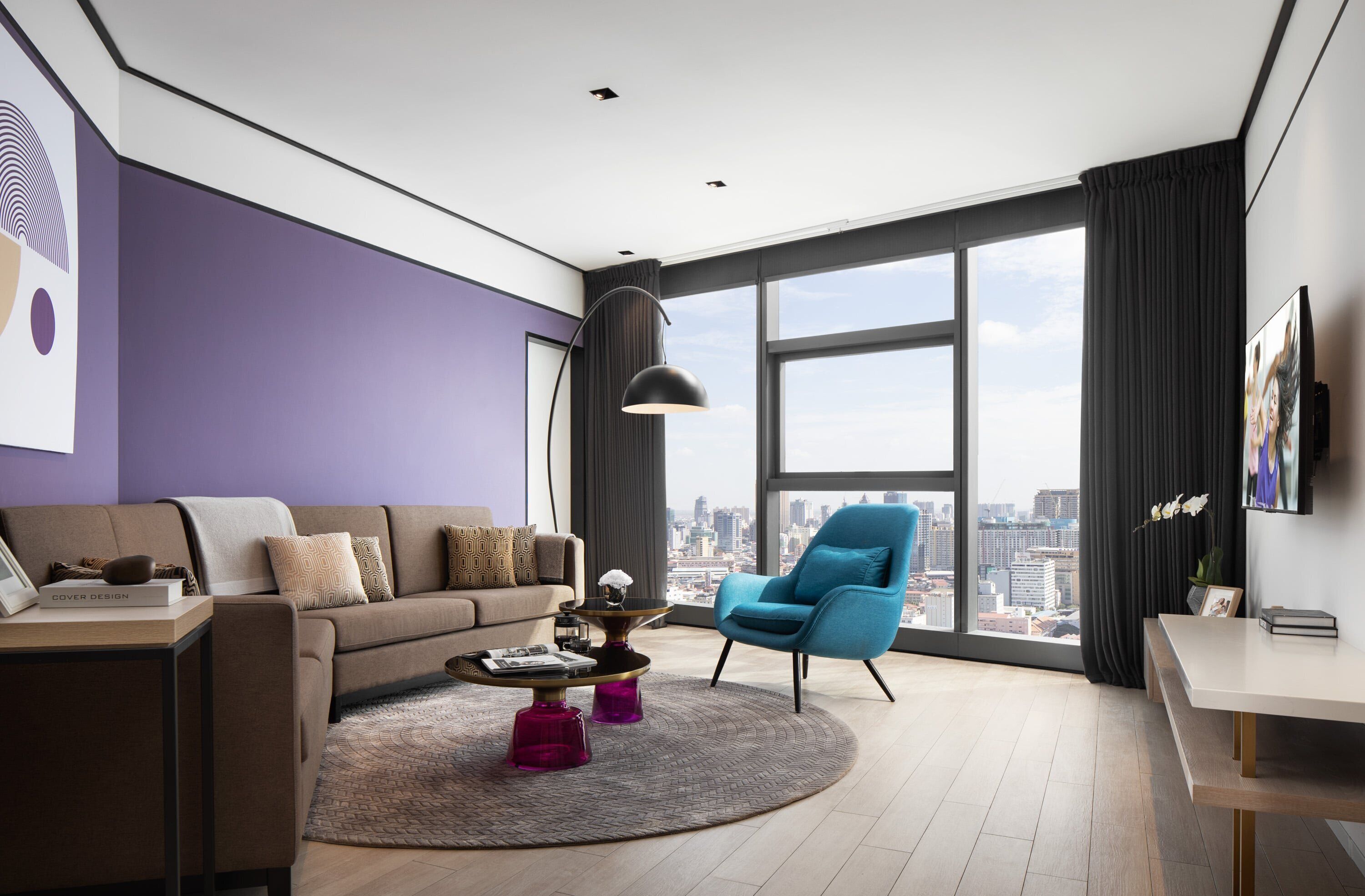 Een moderne woonkamer met een bank, fauteuil, salontafel en een groot raam met uitzicht op de stad.