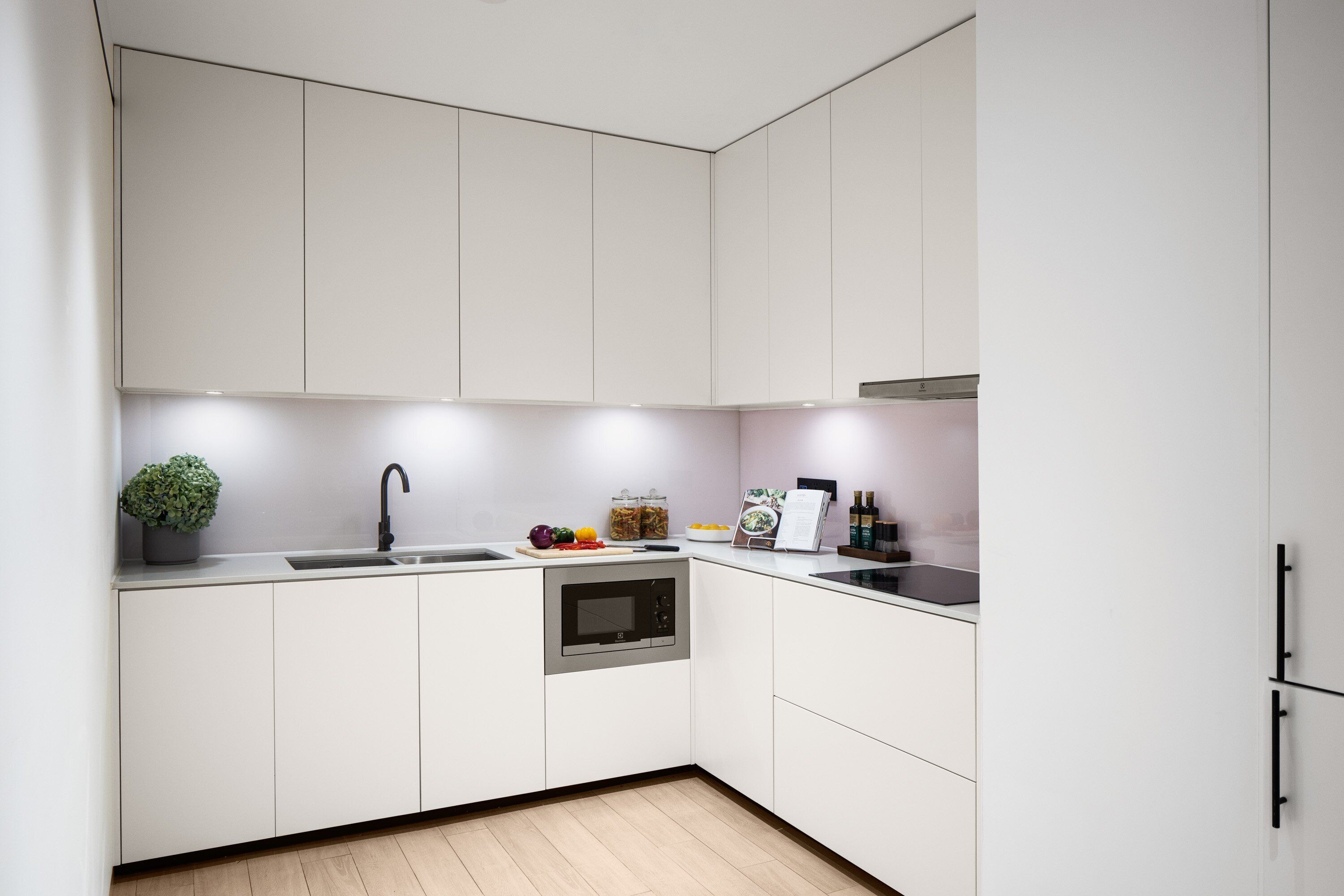 Eine moderne Küche mit weißen Schränken, einem Backofen, einer Spüle und einer Arbeitsplatte mit einem Blumentopf.