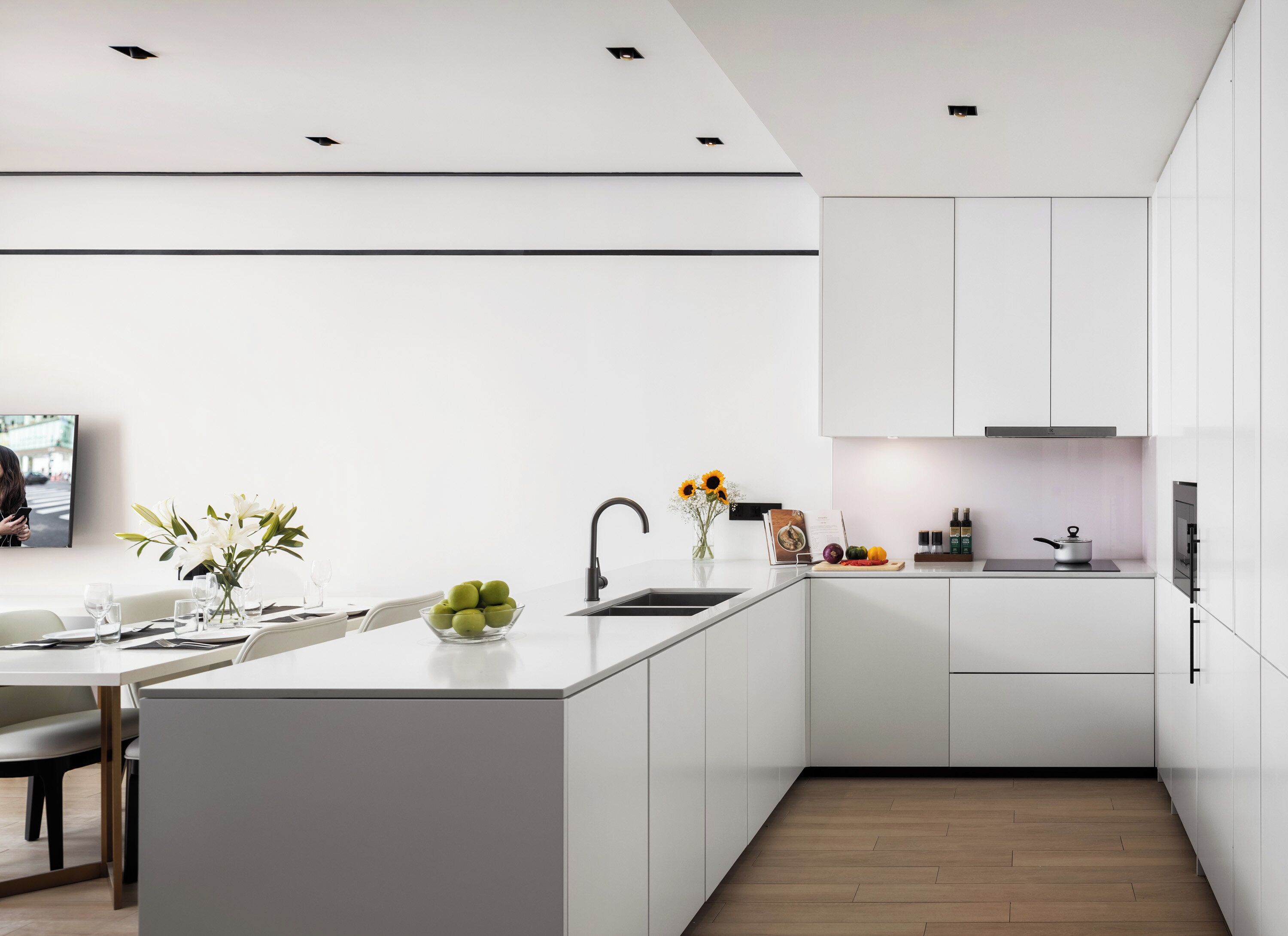 A modern kitchen with white cabinetry, a central island with a bowl of fruit, a sink, and a stove.