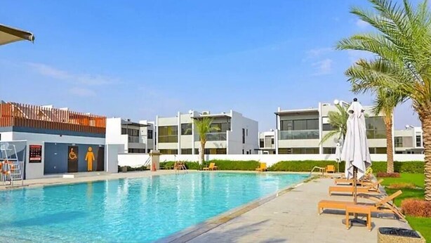 A swimming pool area with lounge chairs, a disabled access sign, and modern buildings in the background. - Luxurious 3 Bedrooms with Maid room Villa (دبي)