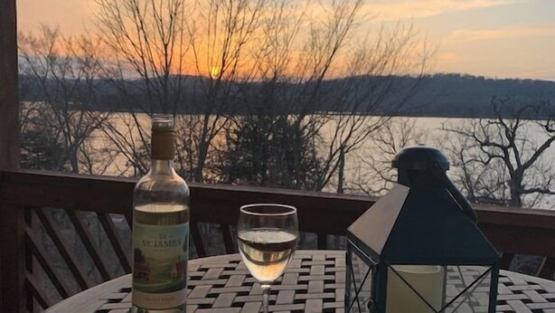 Une table avec une bouteille de vin de Saint-Jacques, un verre de vin blanc, une bougie et une assiette de nourriture, le tout placé sur un balcon donnant sur un coucher de soleil.