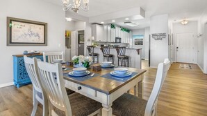 Un coin repas avec une table en bois dressée pour quatre personnes, des chaises blanches et un lustre.
