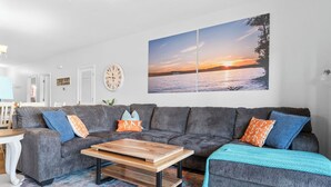 Un salon avec un canapé gris, une table basse en bois et un grand tableau représentant un coucher de soleil, accroché au mur.
