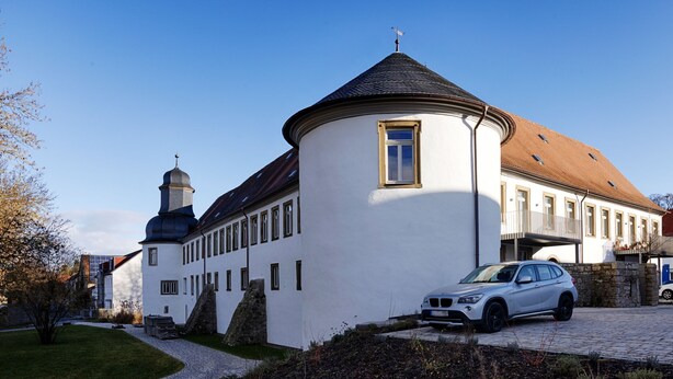 A white building with a round tower and a car parked in front. - homie stay am schloss (Würzburg)