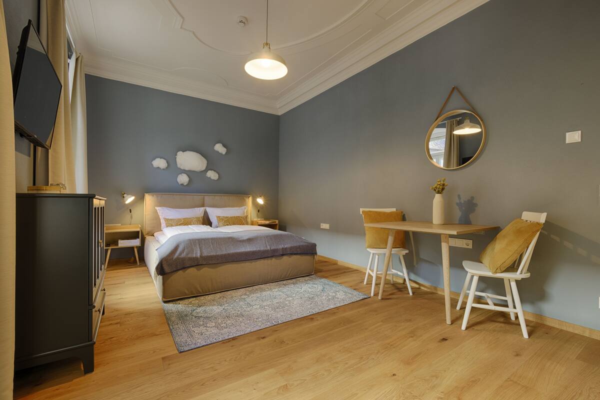 Une chambre à coucher comprenant un lit, des tables de chevet, un bureau avec des chaises, un miroir et une étagère fixée au mur.