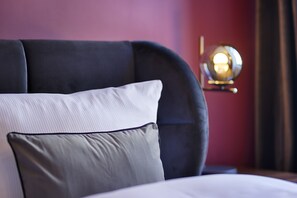 A close-up of a bed with a dark headboard and two pillows, a wall lamp, and a red wall. - homie stay am schloss (Würzburg)