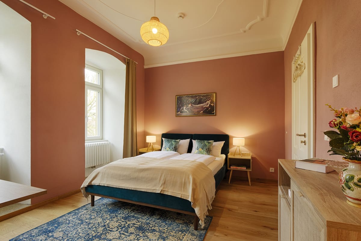 Une chambre à coucher avec un lit, des tables de chevet, une commode, une fenêtre et un tableau accroché au mur.