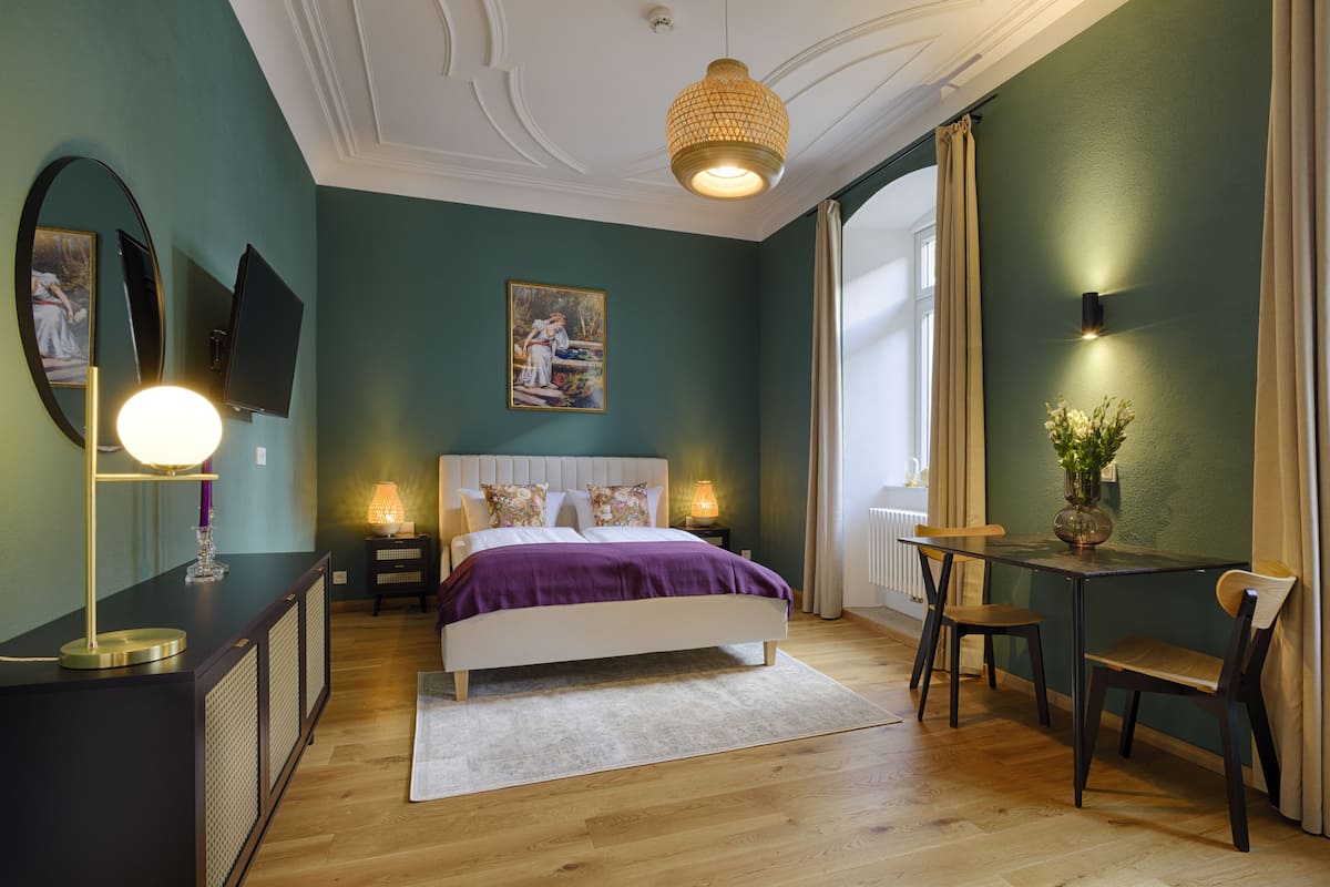 Une chambre à coucher avec un lit, des lampes de chevet, un bureau avec une chaise, un miroir et un tableau accroché au mur.