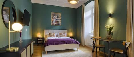 A bedroom with a bed, bedside lamps, a desk with a chair, a mirror, and a painting on the wall.