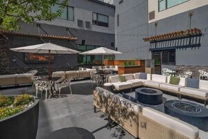 An outdoor seating area with multiple tables and chairs, a fire pit, and a large TV screen.