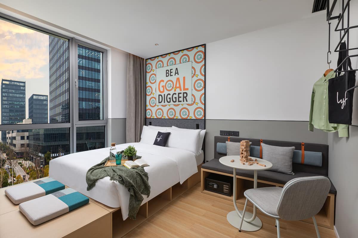 A modern hotel room with a large bed, a small sofa, a round table, and a city view.