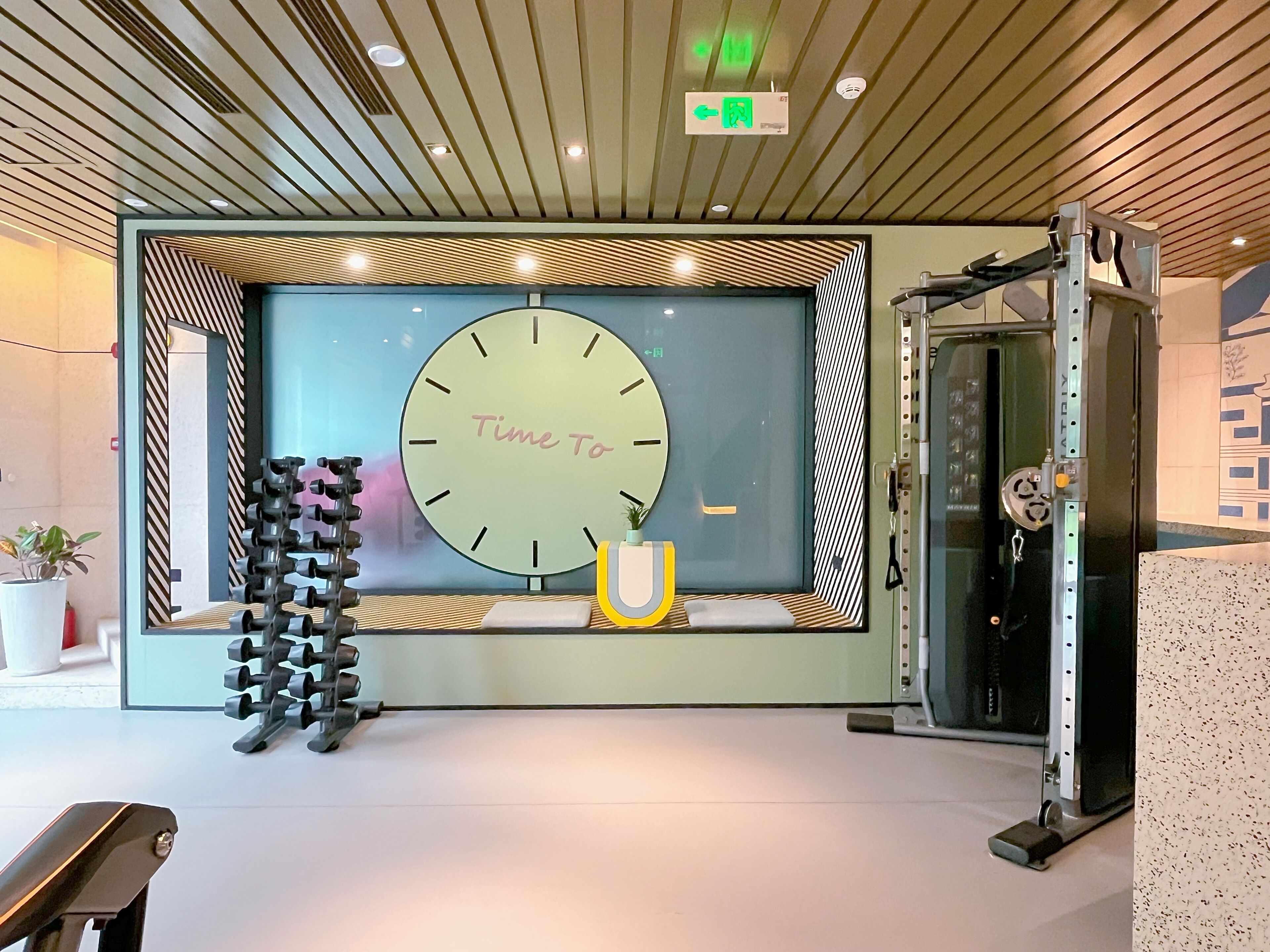Un intérieur moderne avec une grande horloge indiquant l’heure et un espace dédié à la musculation, équipé de divers appareils d’exercice.