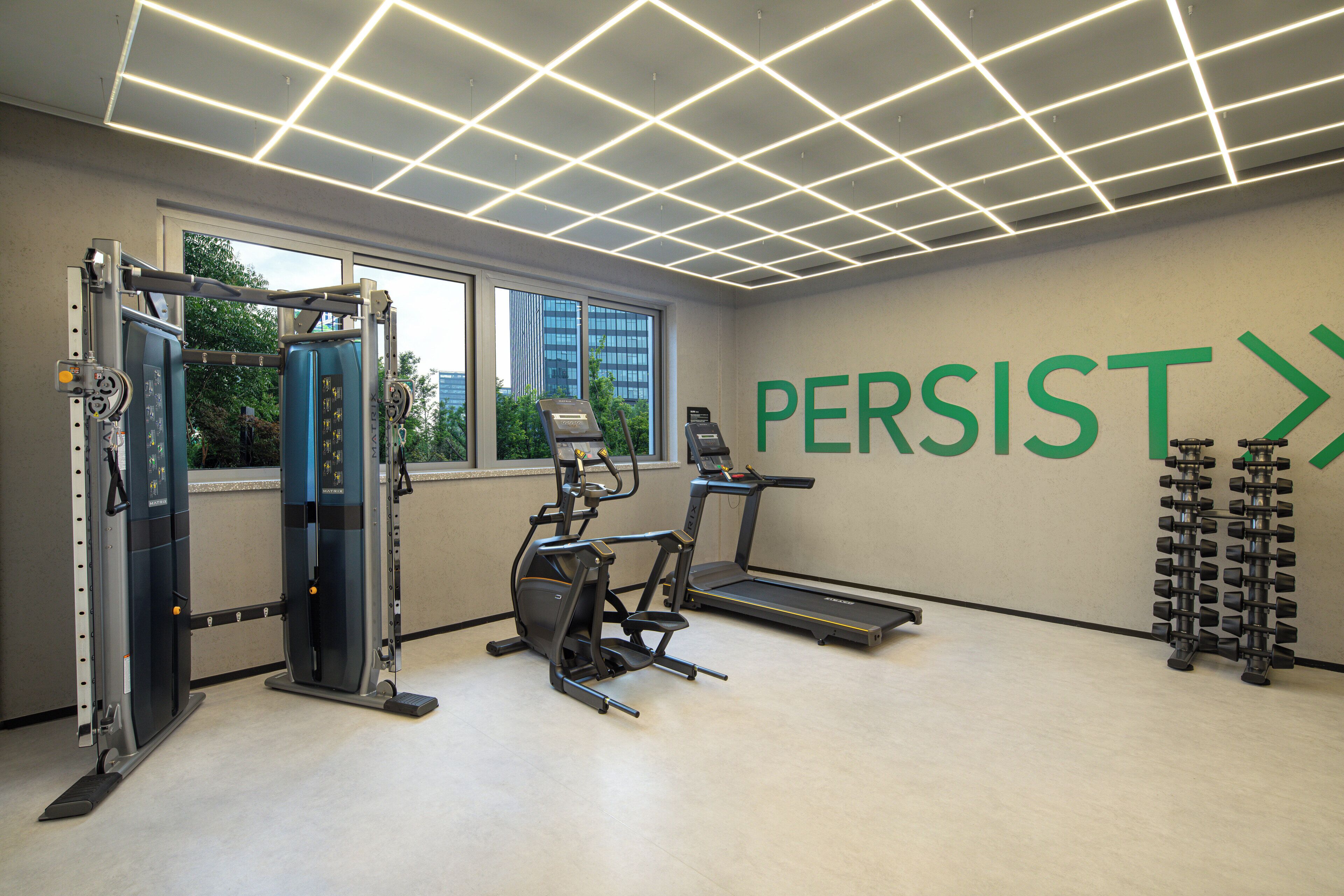 Un gimnasio con equipo de ejercicio, una cinta de correr y una pared con la palabra 'PERSIST'.