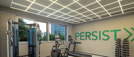 Un gimnasio con equipo de ejercicio, una cinta de correr y una pared con la palabra 'PERSIST'.