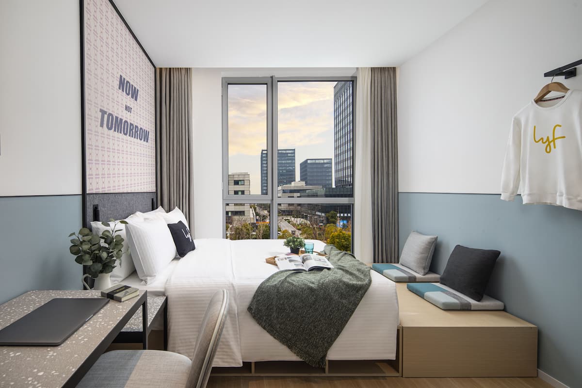 A modern hotel room with a bed, seating area, and a view of the cityscape.