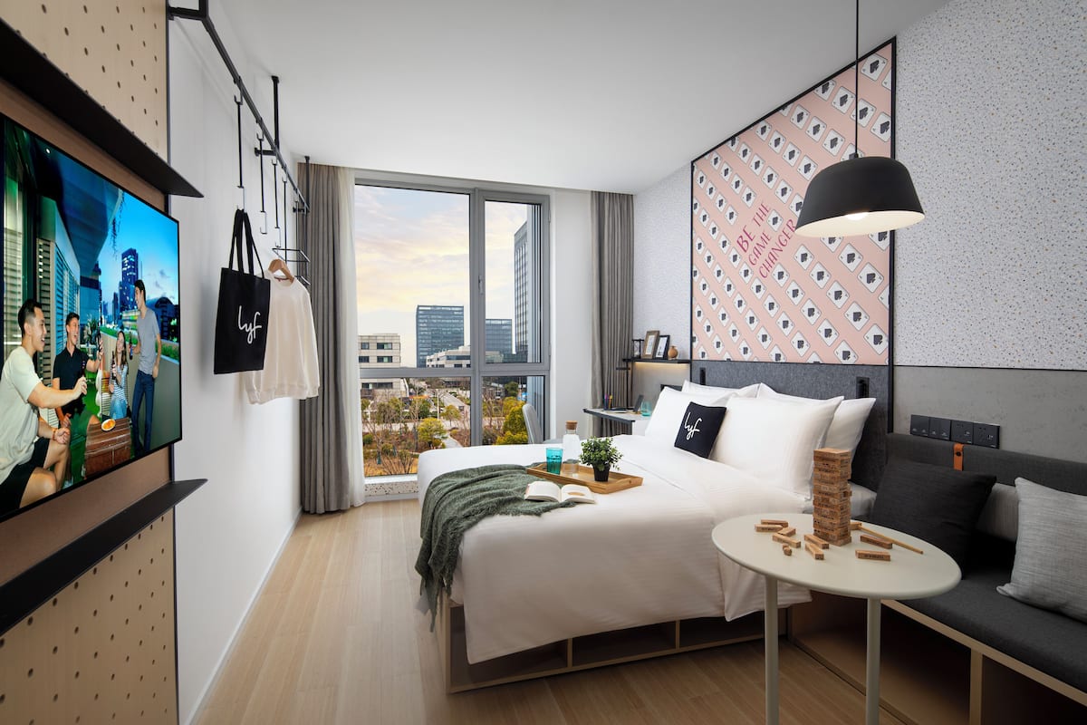 A modern hotel room with a large bed, a small table, a sofa, a TV, and a city view.