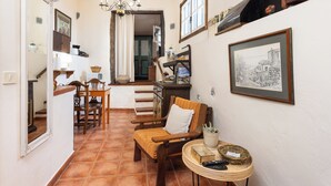 Un couloir étroit avec un coin repas, une chaise en bois avec un coussin, une petite table ronde avec un panier, et une photo en noir et blanc encadrée accrochée au mur.