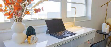 Un espacio de trabajo con una computadora portátil sobre un escritorio blanco, un florero con flores y una pequeña planta.