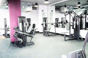 A gym with various exercise machines, a pink pillar, and a mirrored wall. - NEW! Luxury Ocean View  – 1Bd 2Bth – Designer Made & Breathtaking Views (Miami Beach)