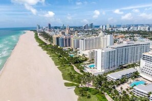 A coastal cityscape with a beachfront hotel featuring multiple high-rise buildings, a swimming pool, and lush greenery.