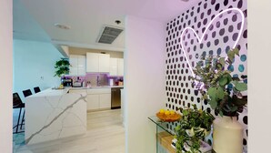 A modern kitchen with white cabinets, a marble countertop, and a glass coffee table. - NEW! Luxury Ocean View  – 1Bd 2Bth – Designer Made & Breathtaking Views (Miami Beach)