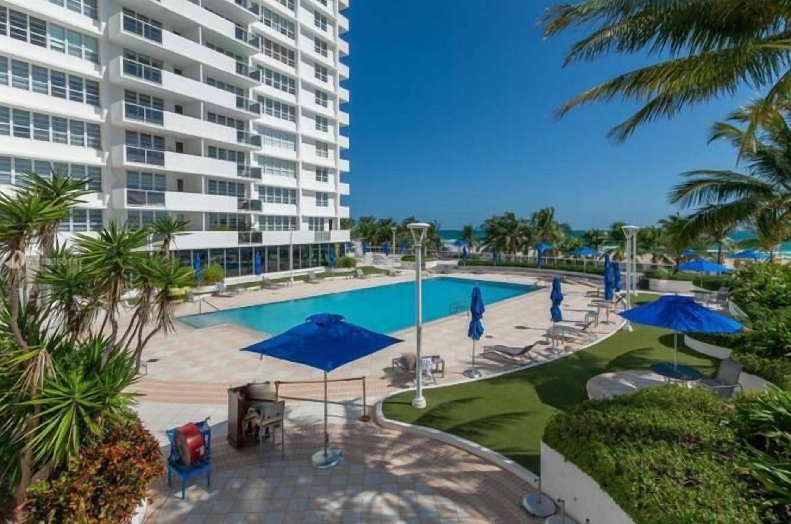A hotel with a pool, outdoor seating, and palm trees.