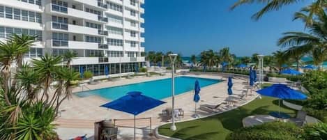 A hotel with a pool, outdoor seating, and palm trees.
