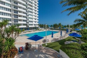 A hotel with a pool, outdoor seating, and palm trees. - NEW! Luxury Ocean View  – 1Bd 2Bth – Designer Made & Breathtaking Views (Miami Beach)