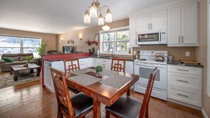 Une cuisine moderne avec des meubles blancs, une table à manger avec des chaises, un lustre et une vue sur l’extérieur.